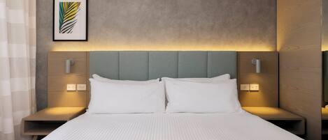 A modern hotel room with a large bed, two bedside tables, a headboard, and a framed artwork on the wall.