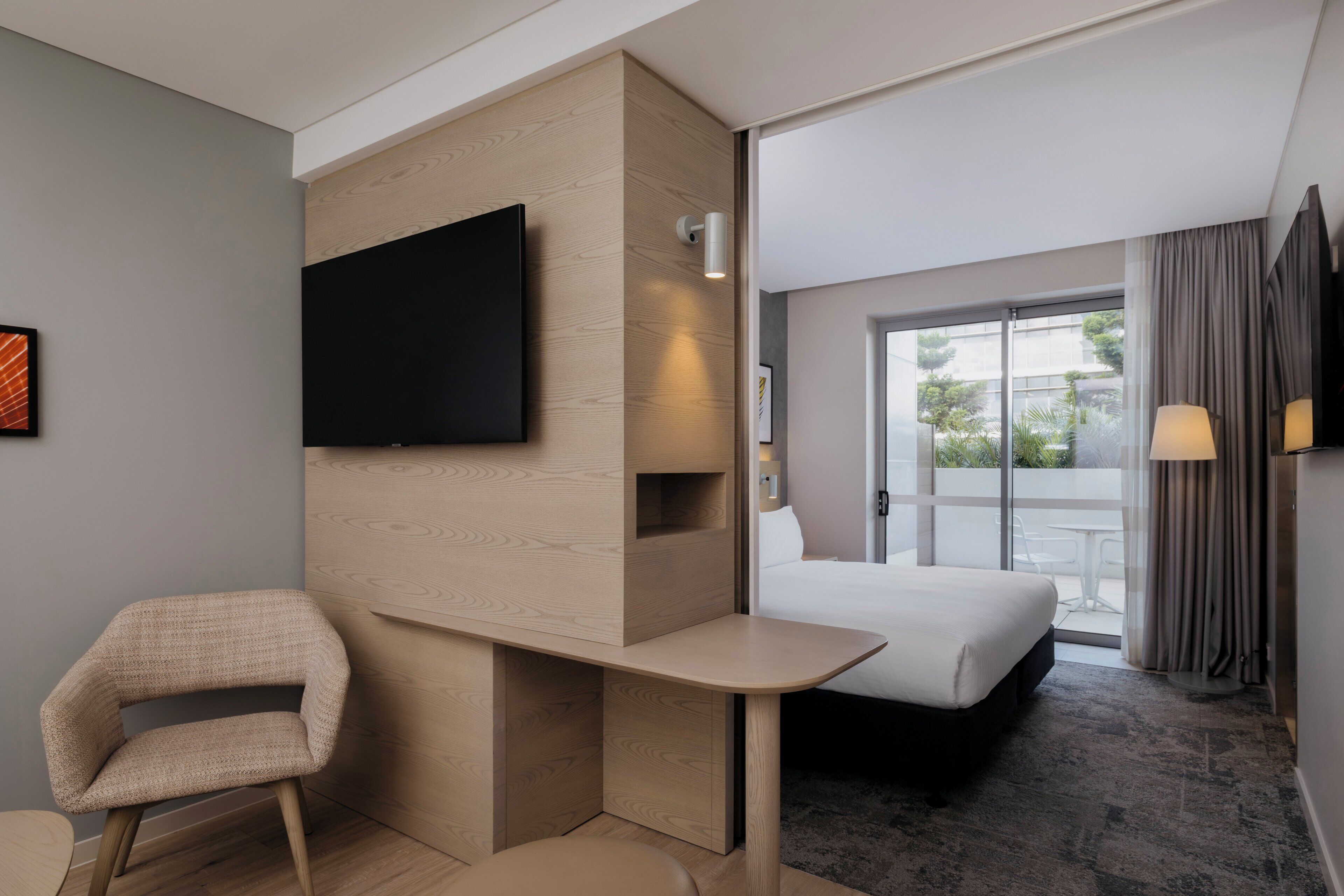 Une chambre d’hôtel avec un lit, un bureau, une chaise, une télévision et une fenêtre avec des rideaux.