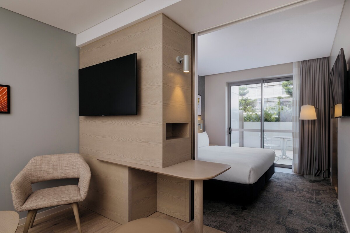 A hotel room with a bed, a desk, a chair, a TV, and a window with curtains.