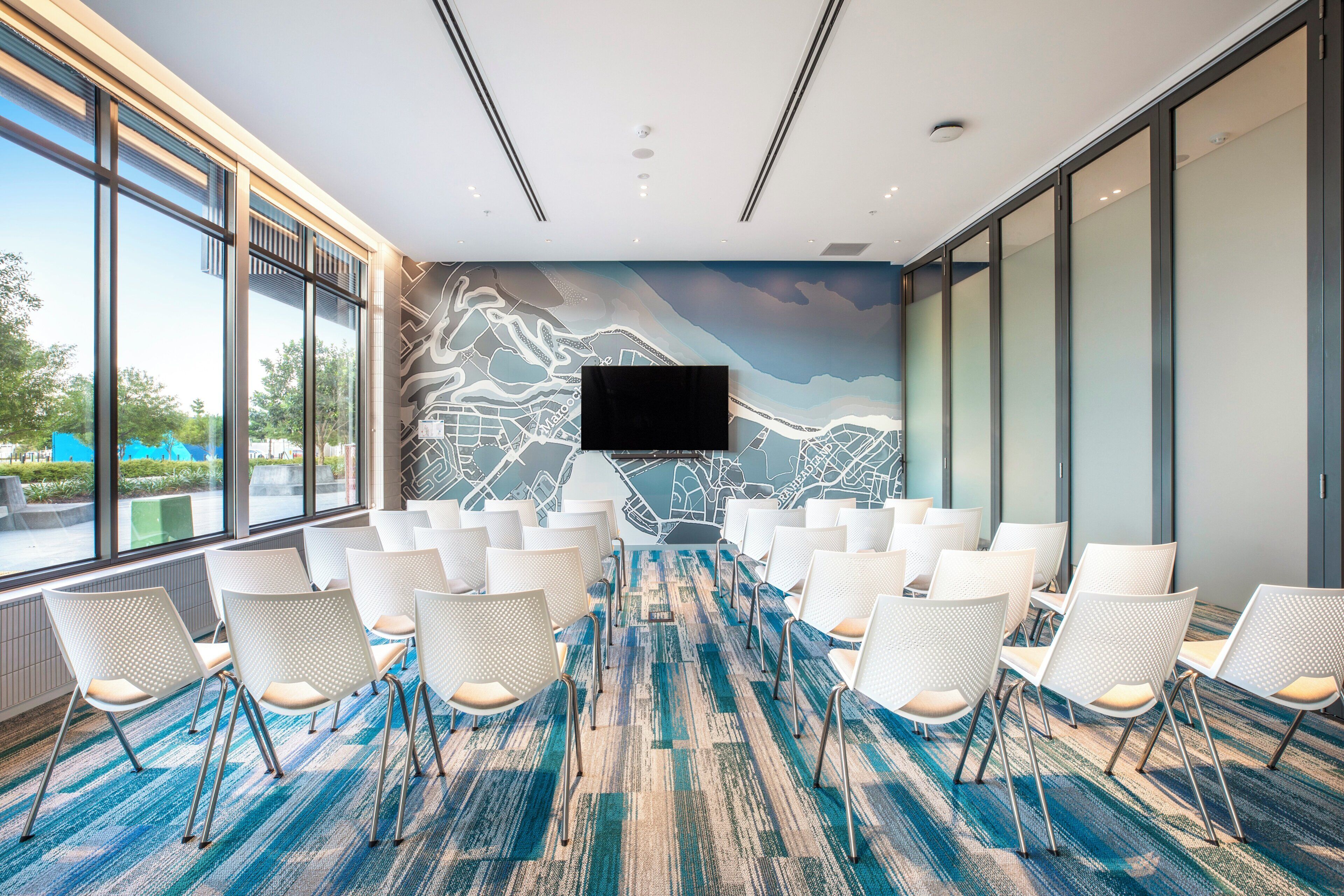 A conference room with a large screen, white chairs, and a carpeted floor.