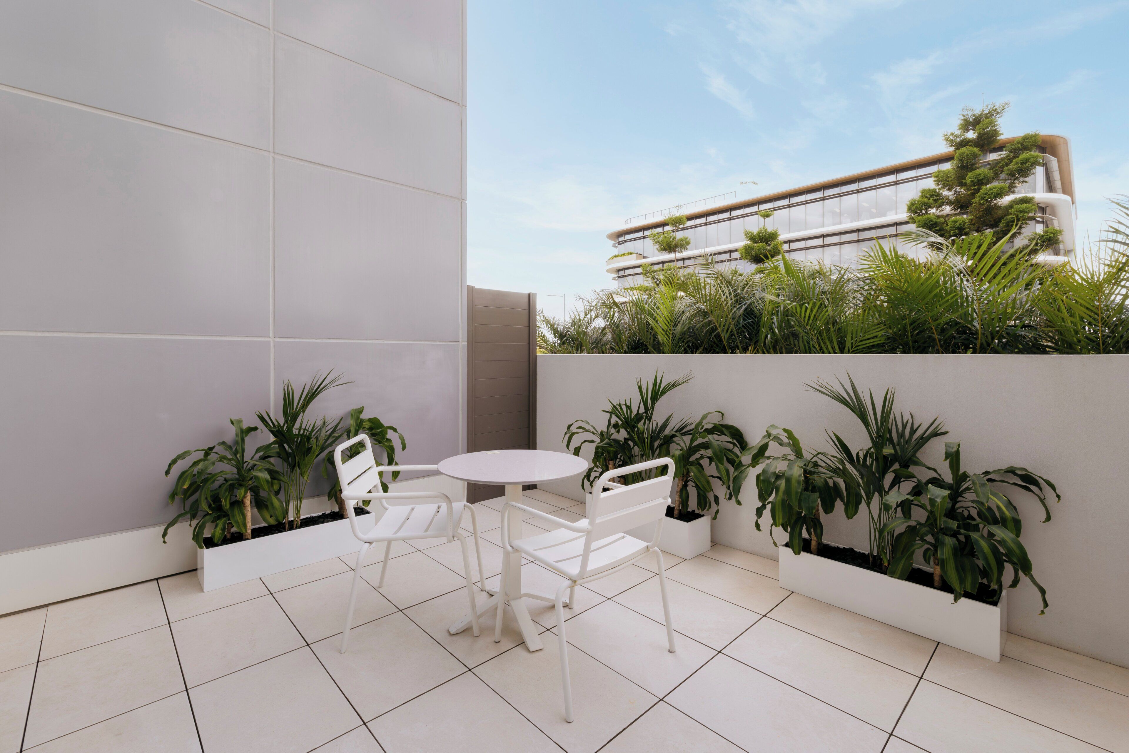 A modern outdoor seating area with white chairs and a table, surrounded by potted plants.