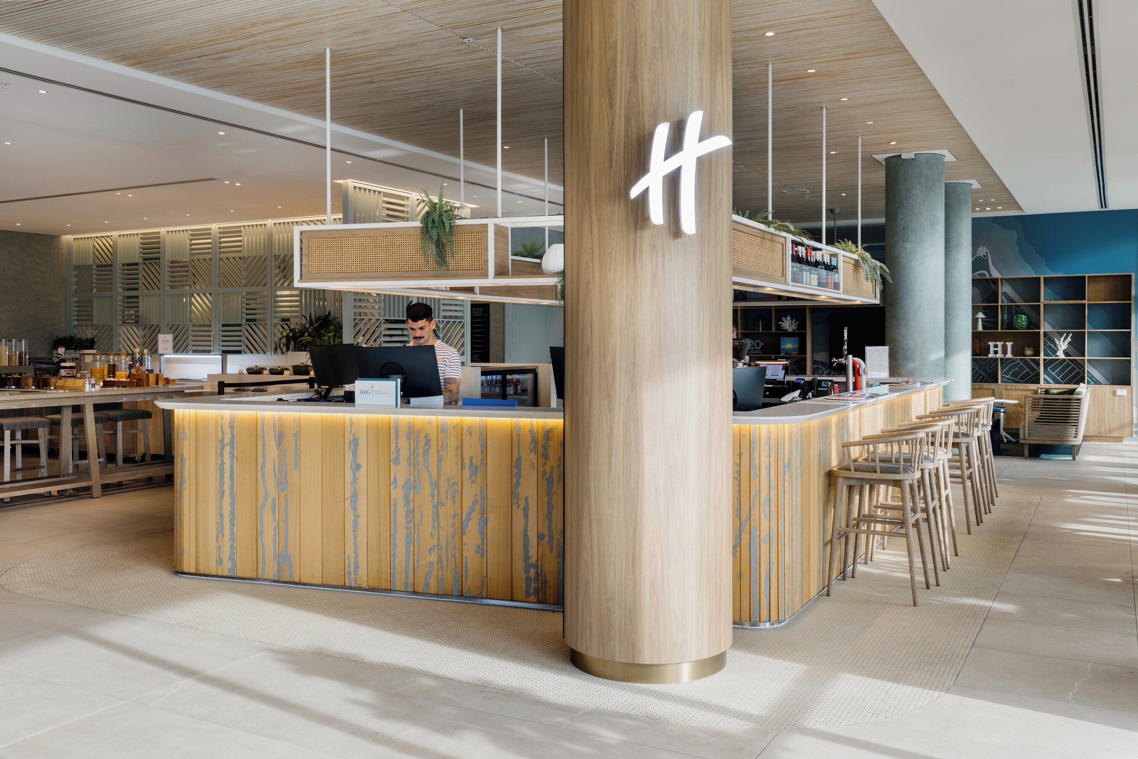A modern bar area with a wooden counter, bar stools, and a large pillar with a sign.