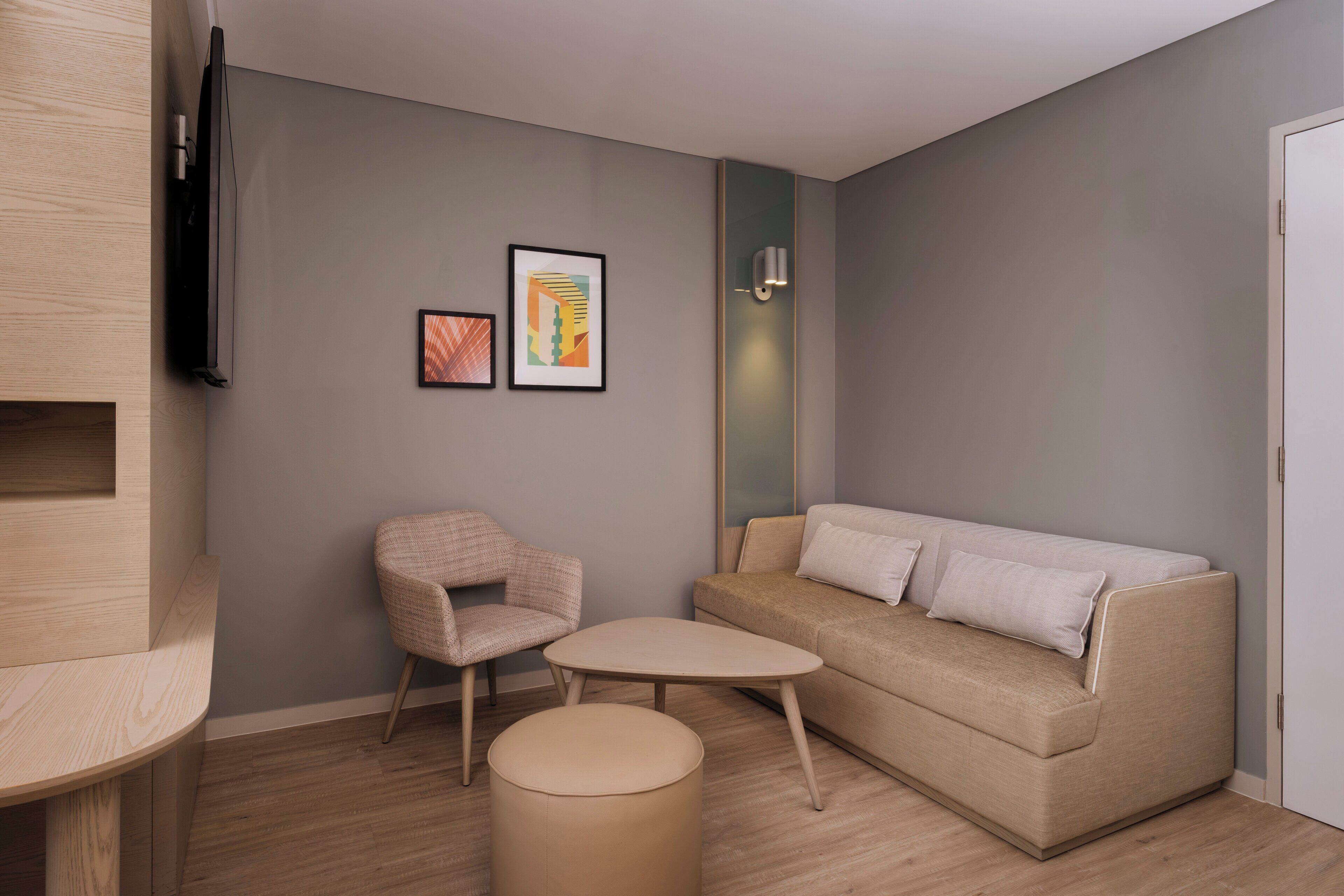 A modern living room with a sofa, a chair, a small table, and a flat-screen TV mounted on the wall.