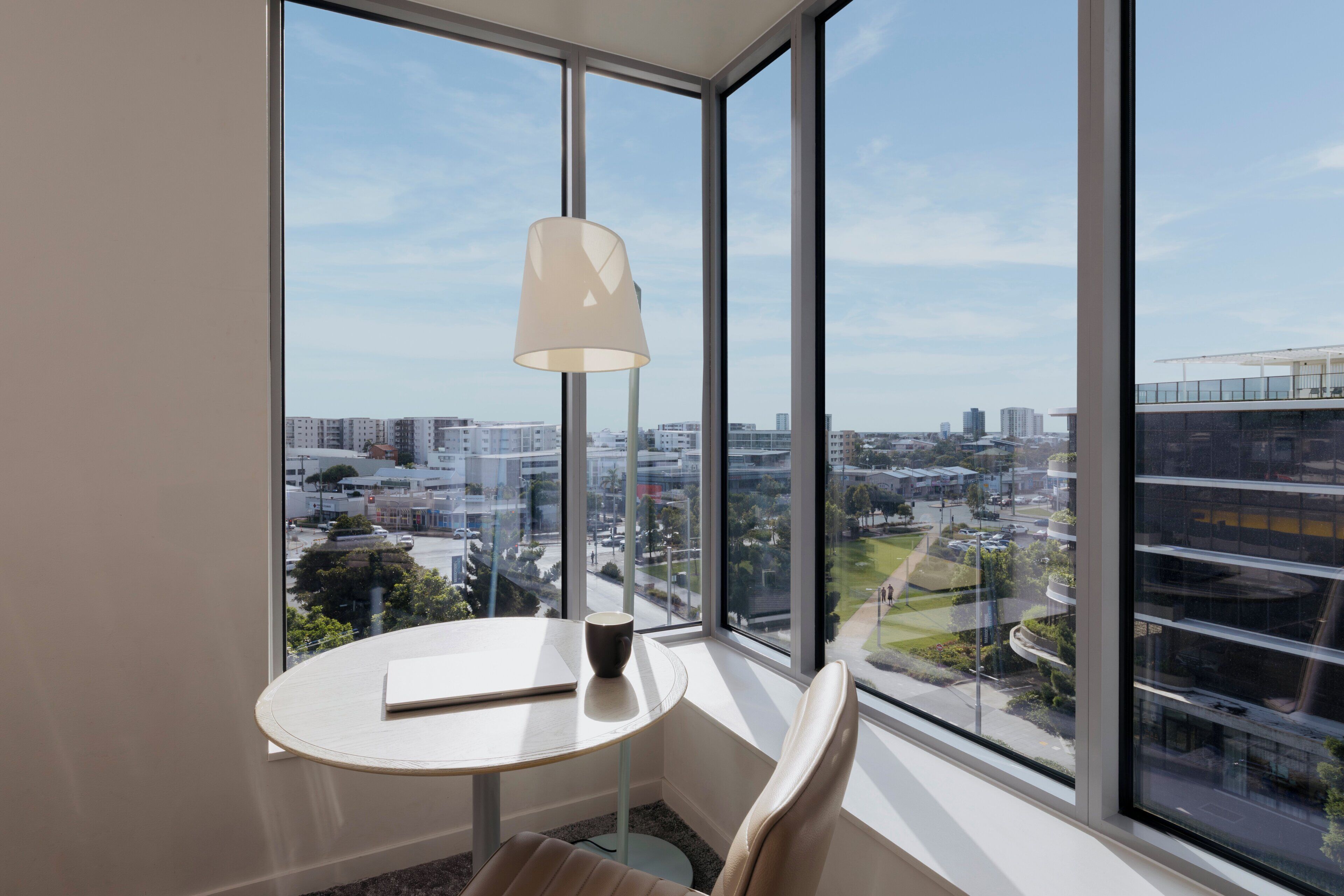 Habitación de esquina con un ventanal grande, una mesa redonda, una silla y una lámpara.