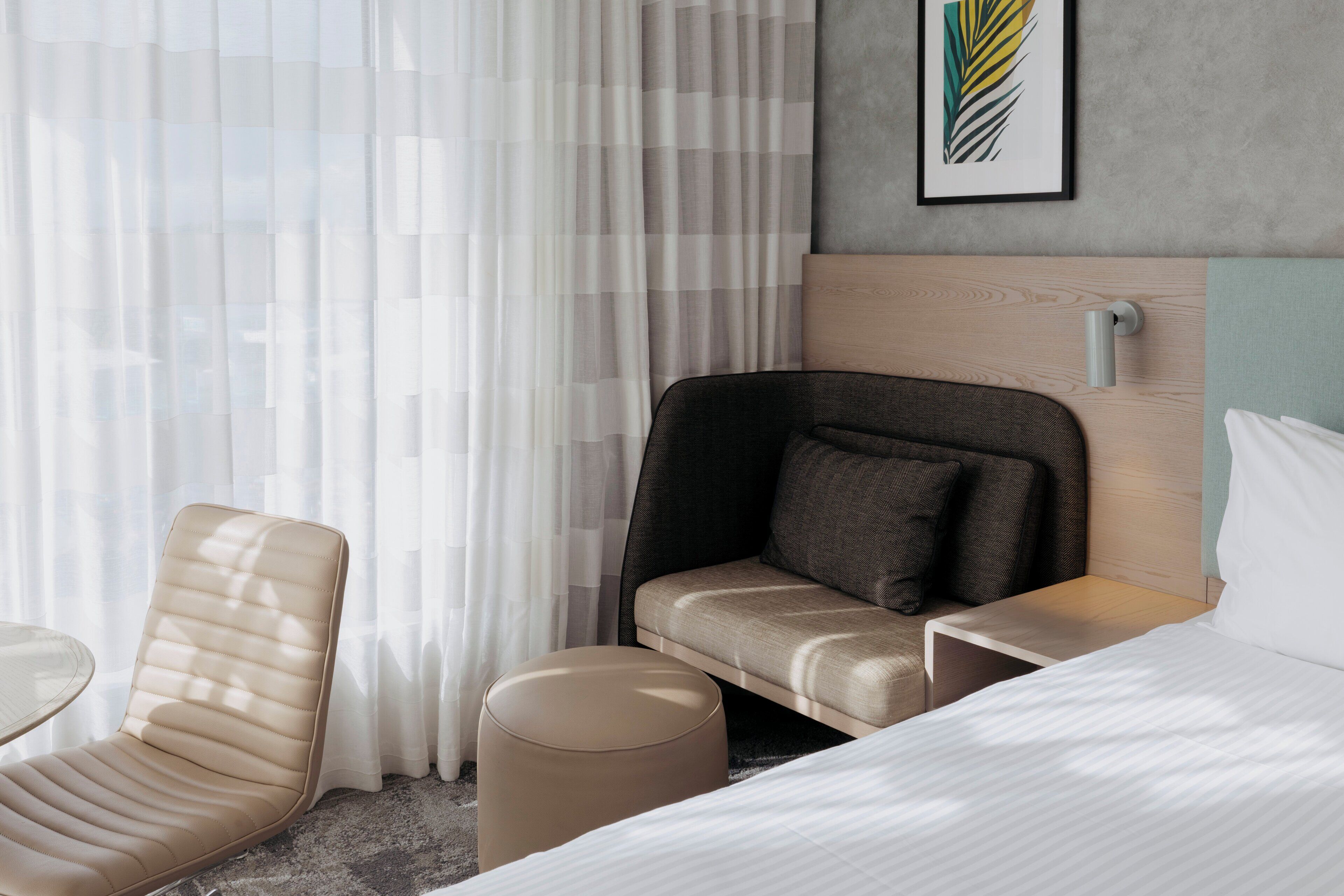 Habitación de hotel con cama, sofá, sillón, mesita pequeña y lámpara de pared.