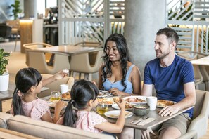 Uma família jantando em um café ao ar livre com design moderno, assentos confortáveis e vista para os arredores.