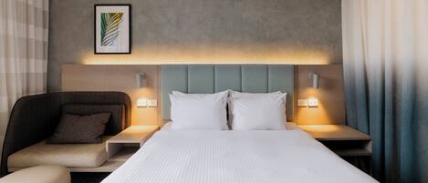 Camera d'albergo con un letto grande, una testiera, due comodini con lampade, una sedia e un'opera d'arte appesa al muro.