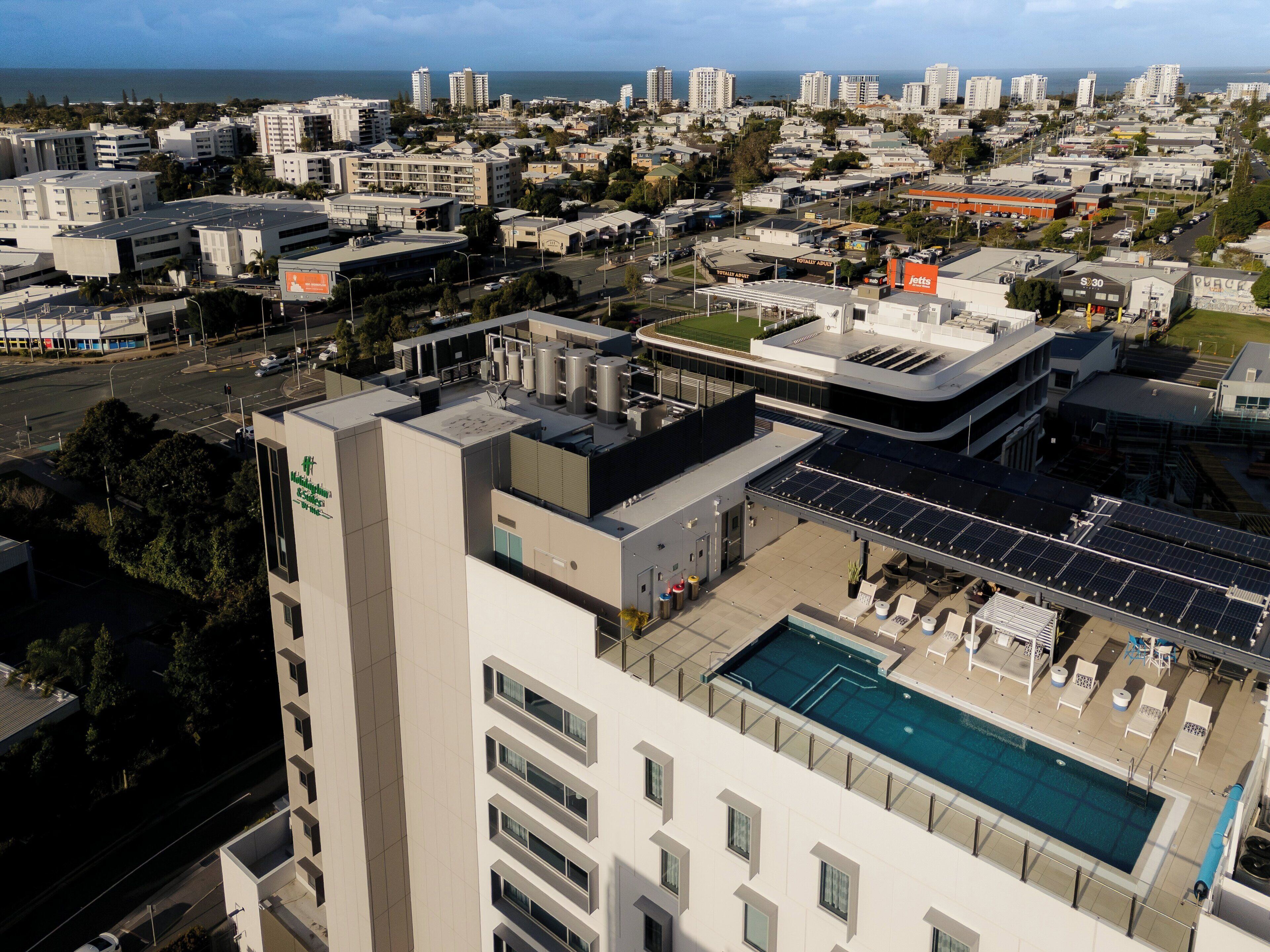A high-rise hotel with a rooftop pool, solar panels, and a view of the cityscape.