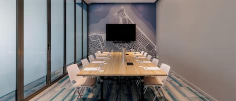 A conference room with a long table, white chairs, a flat-screen TV, and a cityscape mural on the wall.