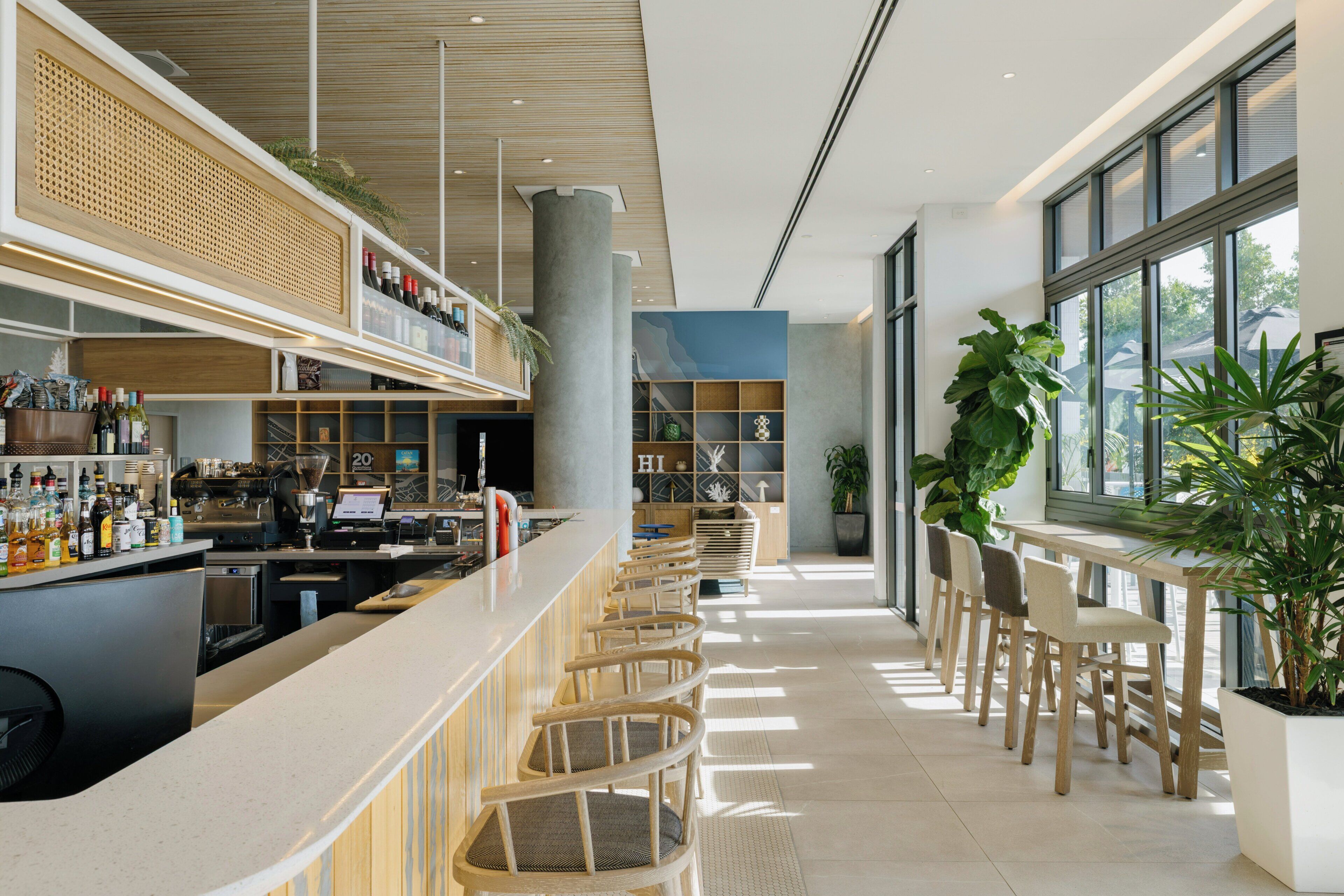 A modern bar area with a long counter, seating, and a large window providing natural light.