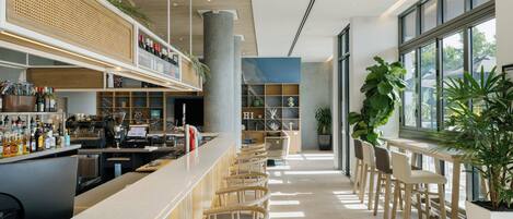 A modern bar area with a long counter, seating, and a large window providing natural light.