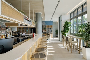 A modern bar area with a long counter, seating, and a large window providing natural light. - Holiday Inn & Suites Sunshine Coast by IHG (Maroochydore)