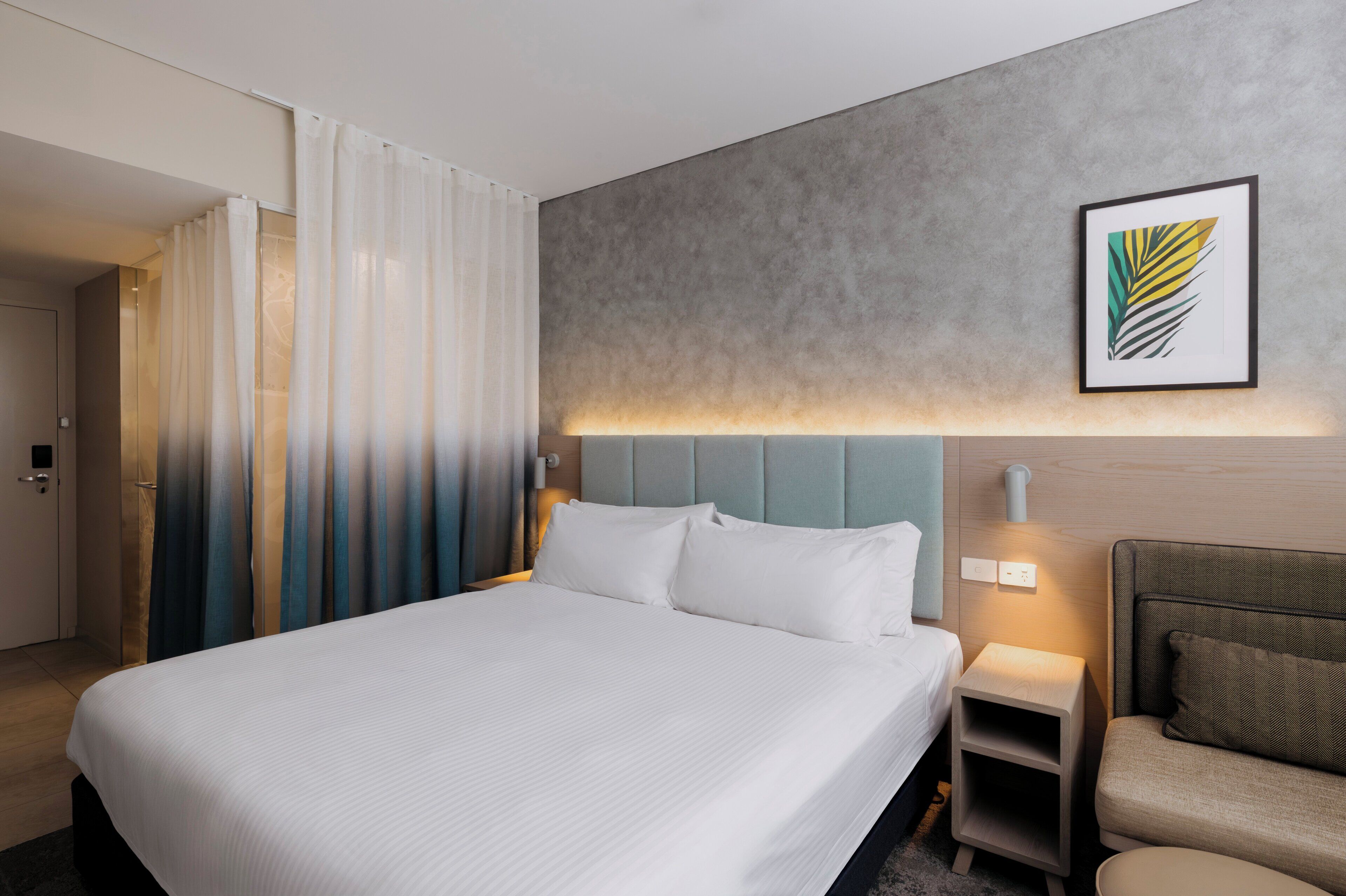 Habitación de hotel con una cama grande, mesitas de noche, un sofá y una obra de arte enmarcada en la pared.
