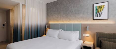 A hotel room with a large bed, bedside tables, a nightstand, a sofa, and a framed artwork on the wall.