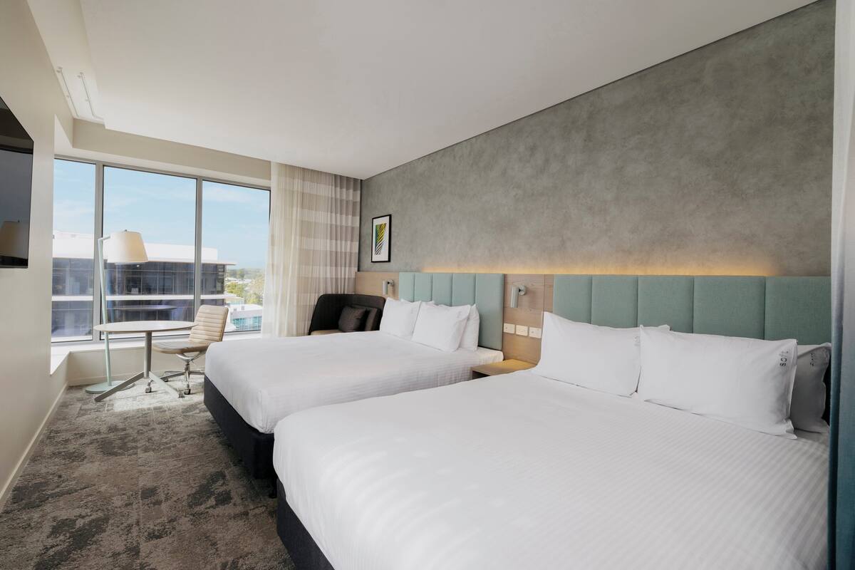 Hotellihuone, jossa on kaksi sänkyä, työpöytä, tuoli ja suuri ikkuna.