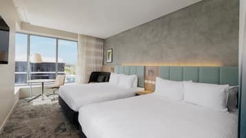 A hotel room with two beds, a desk, a chair, and a large window.