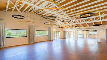 A spacious room with wooden floors, large windows, and a high ceiling with exposed beams and circular light fixtures.