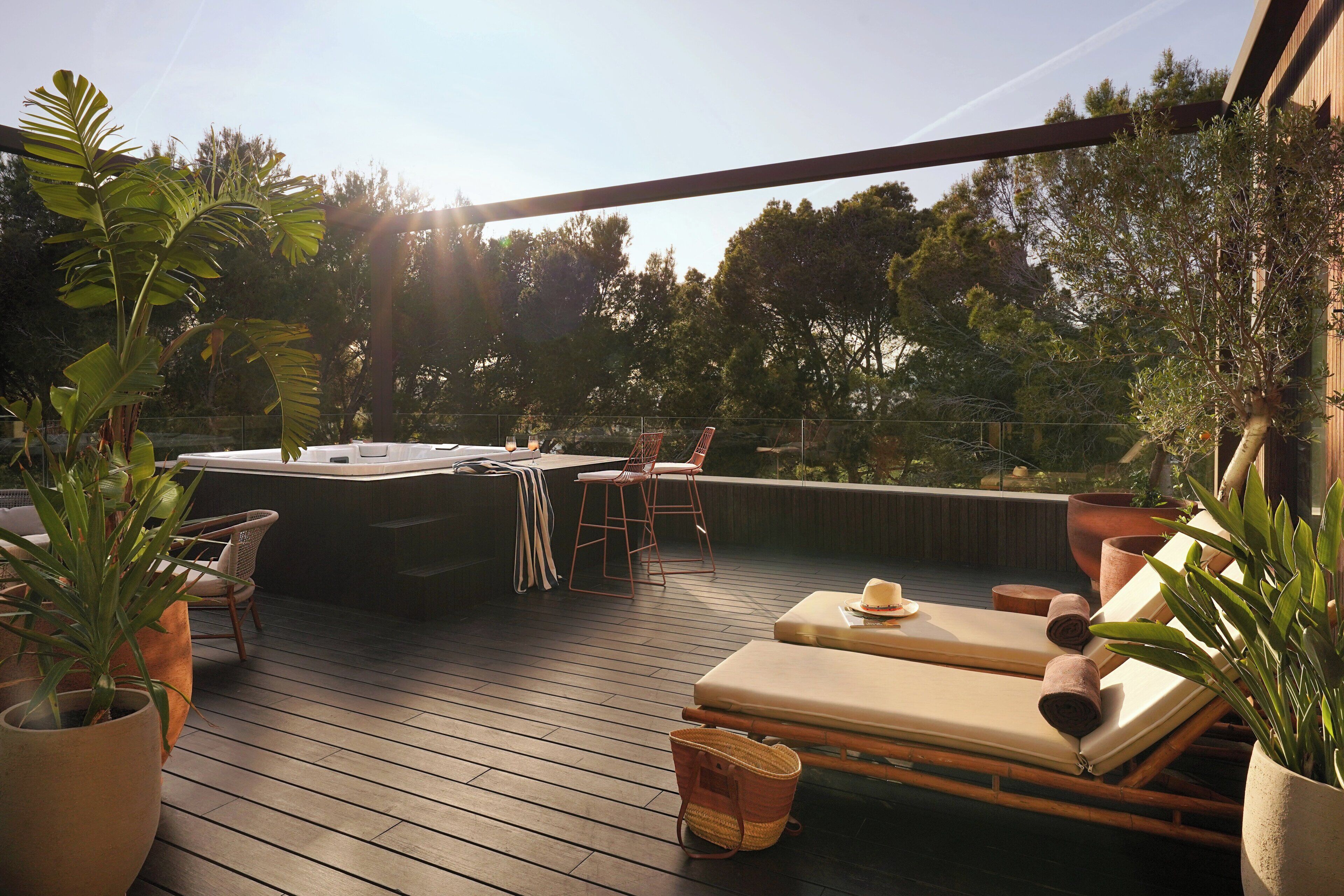 Una terraza de madera con sillas de descanso, un jacuzzi y plantas en macetas.