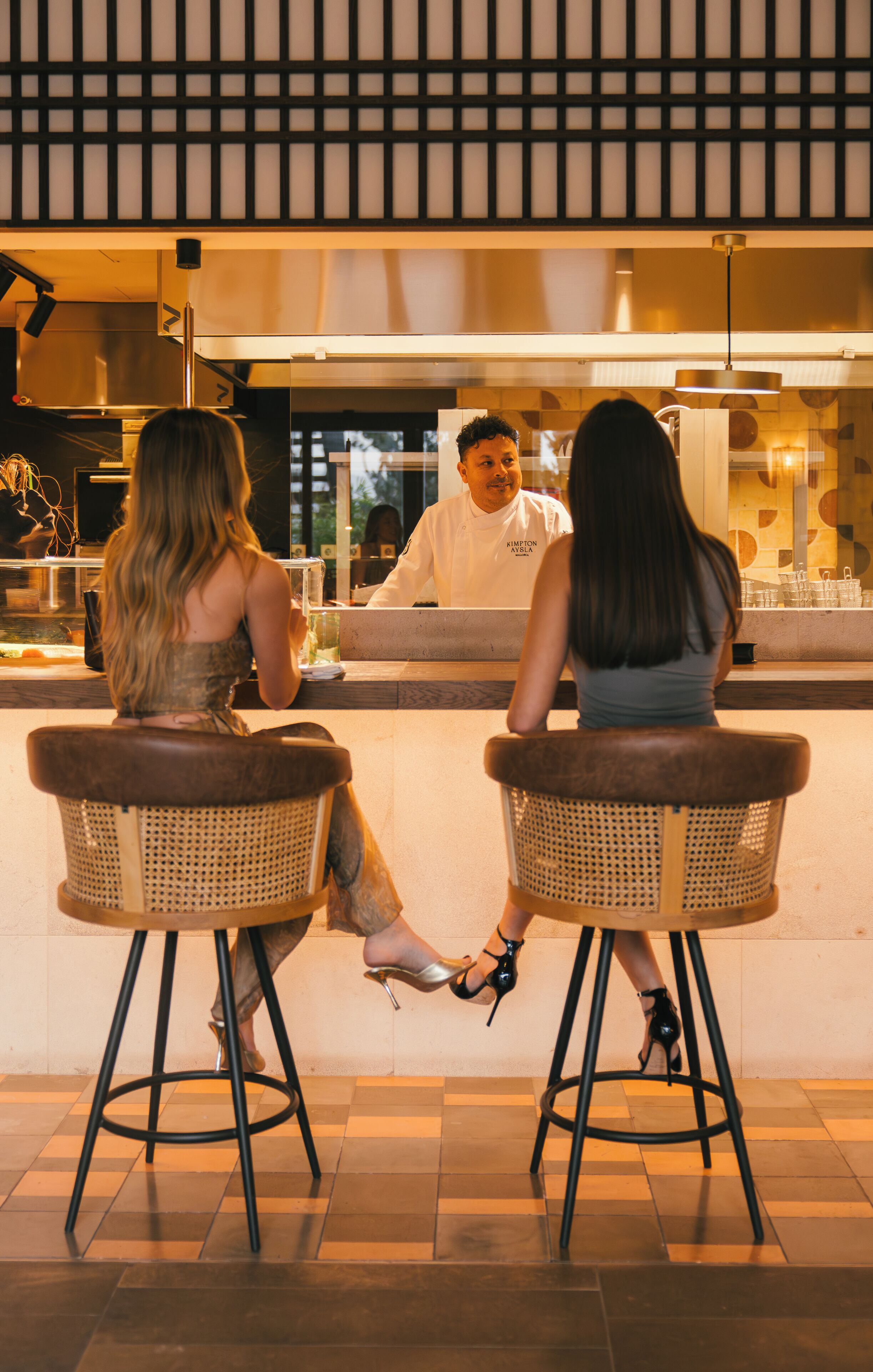 Two people seated at a bar with stools, facing a counter where a server is attending to them.