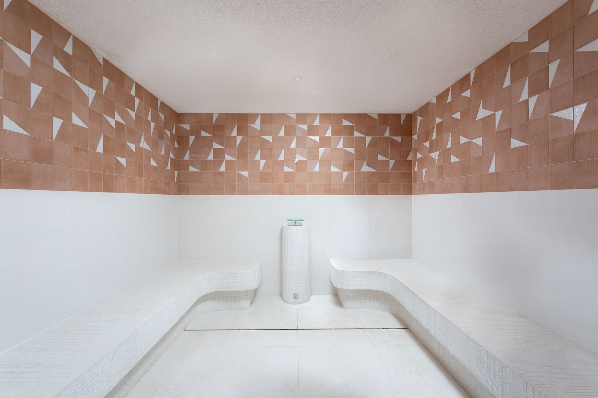 Une salle de spa avec une baignoire blanche, un porte-serviettes et un mur orné de motifs géométriques en carreaux.