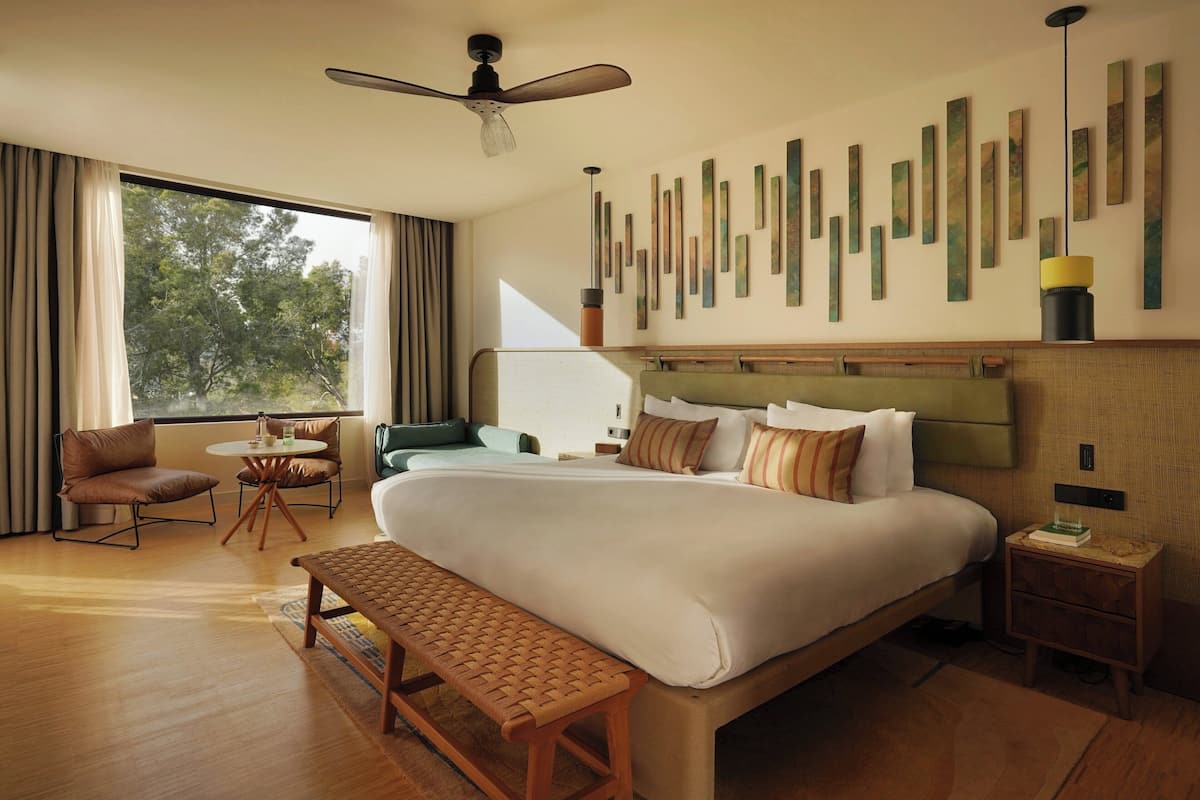 A hotel room with a large bed, a desk, a chair, a bench, and a wall with vertical wooden panels.