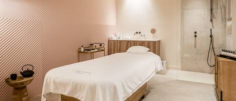 Une chambre moderne avec un lit en bois, une table de chevet, un petit tabouret en bois, un lavabo et un espace douche.