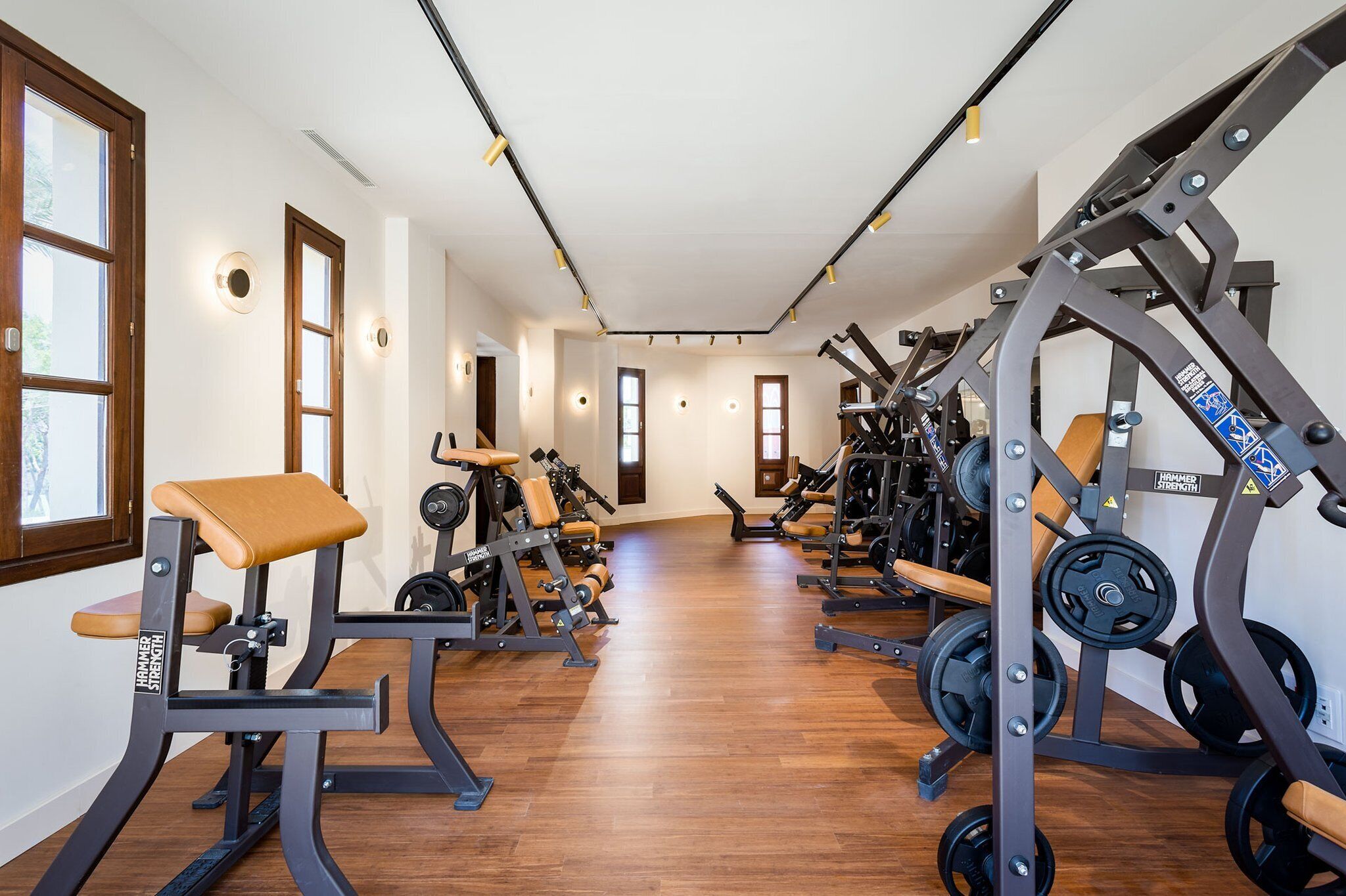 A gym with various exercise equipment, wooden flooring, and large windows.