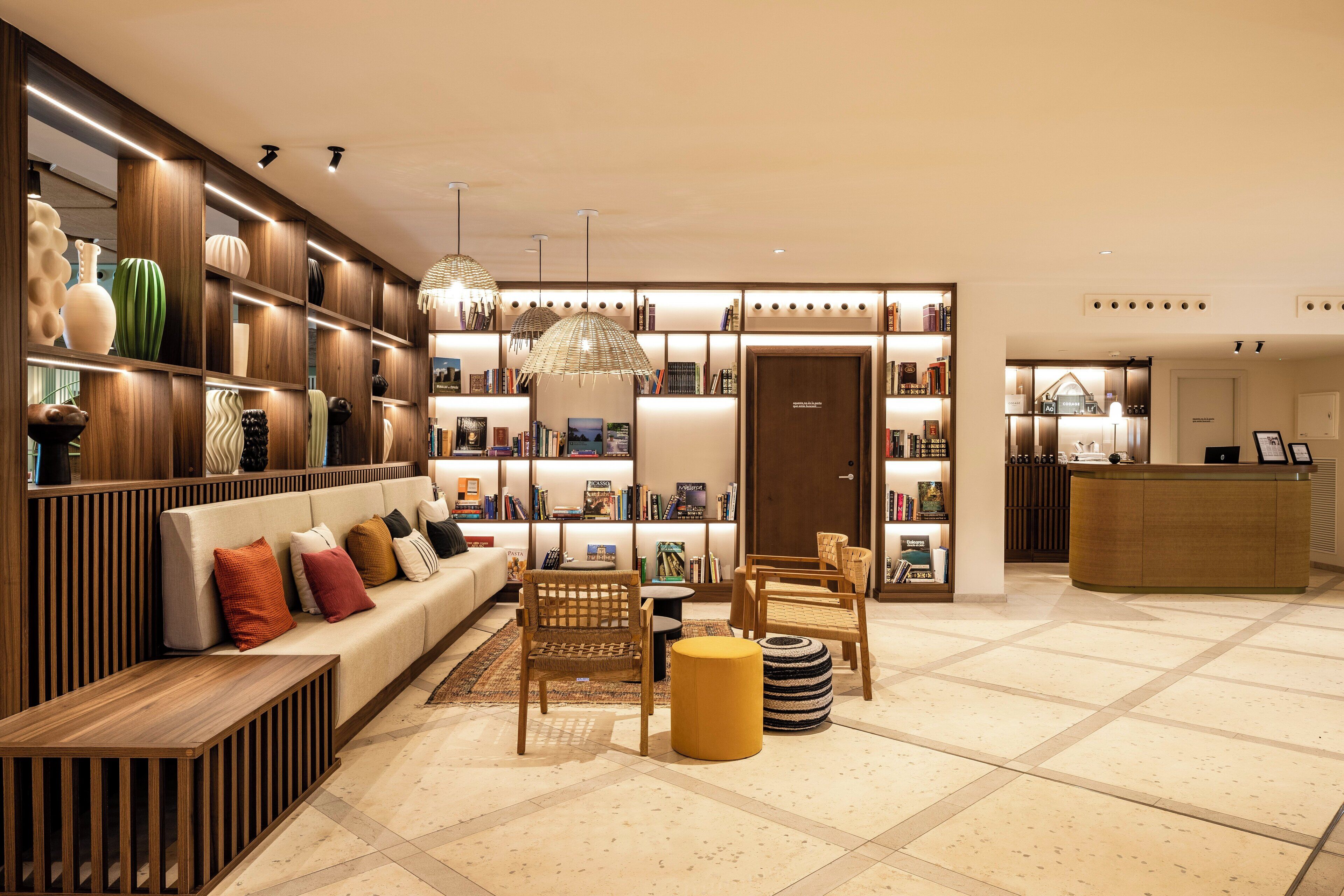 A modern hotel lobby with a sofa, chairs, a reception desk, and bookshelves.