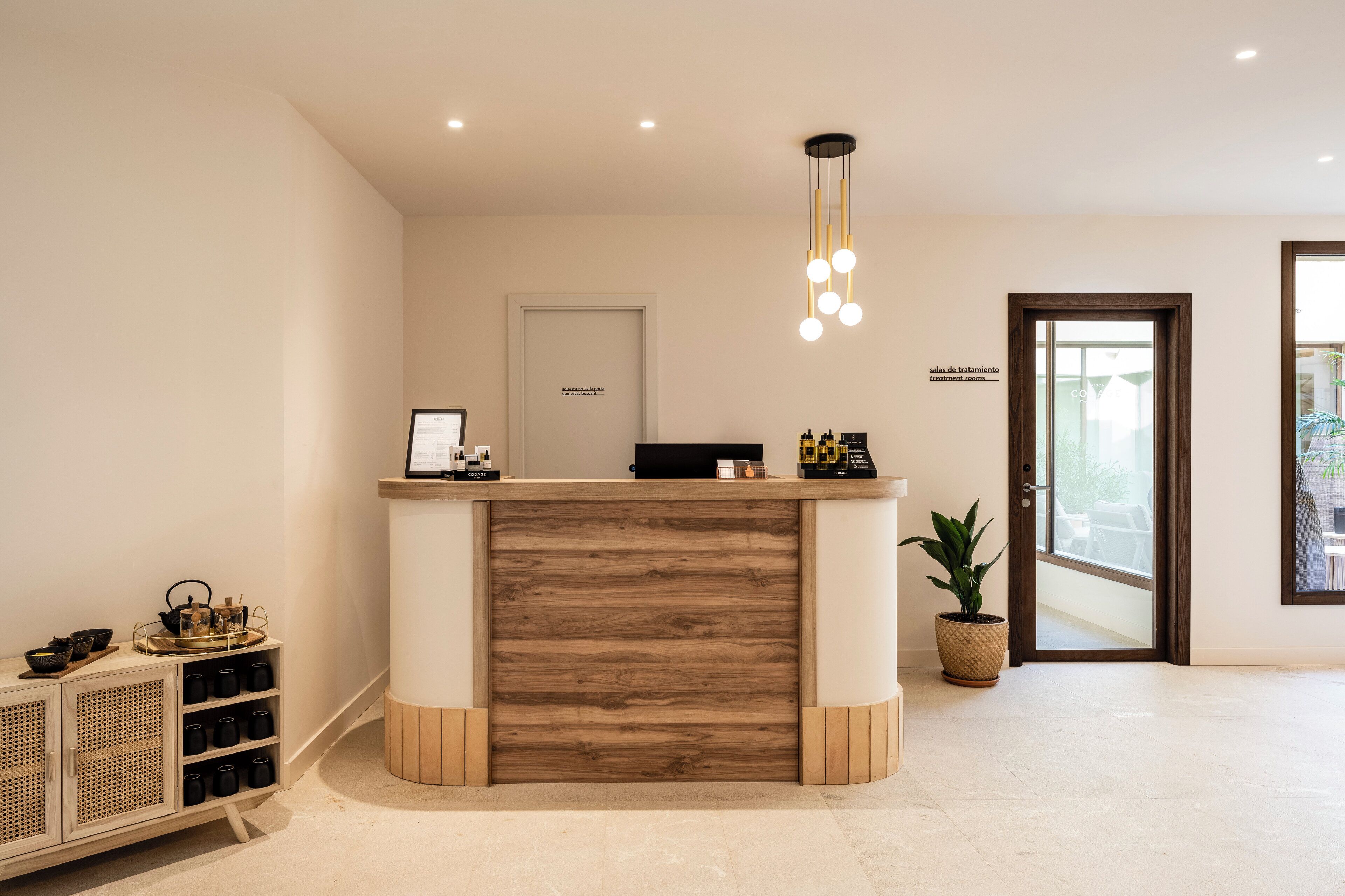 Una recepción con detalles de madera, una planta en maceta y un letrero que indica una sala de tratamientos.