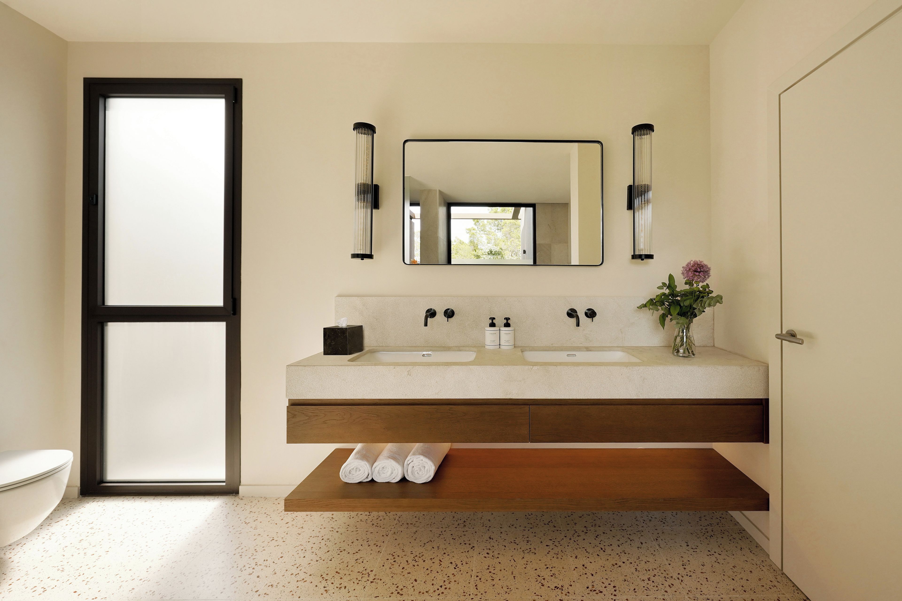 Un baño moderno con lavamanos doble, un espejo grande y un estante de madera debajo del lavabo.