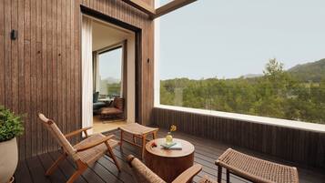 Una terraza de madera con mobiliario de mimbre, una mesa redonda de madera y vistas a un paisaje boscoso.