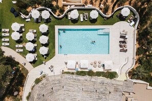 An aerial view of a resort with a central swimming pool, multiple lounge areas with umbrellas, and a well-maintained lawn. - Kimpton Aysla Mallorca by IHG (Calvia)