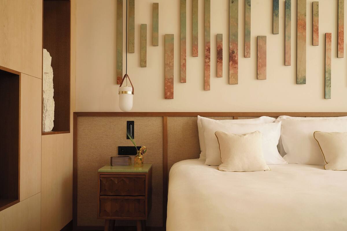 A hotel room with a bed, a nightstand with a vase, and a wall with vertical wooden panels.