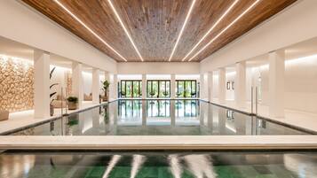 A modern indoor pool area with a wooden ceiling, clear glass walls, and a central water feature.