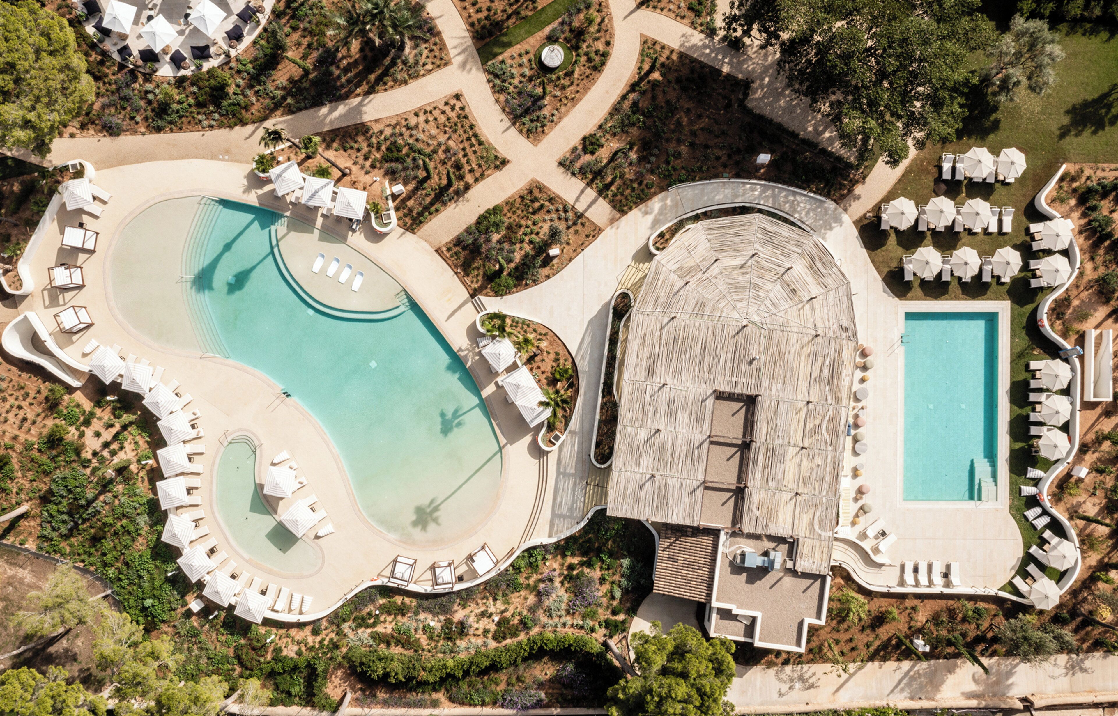 Vista aérea de un resort con múltiples piscinas, tumbonas y zonas sombreadas.