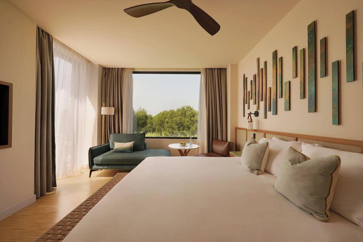 A hotel room with a large bed, a sofa, a small table, and a ceiling fan.