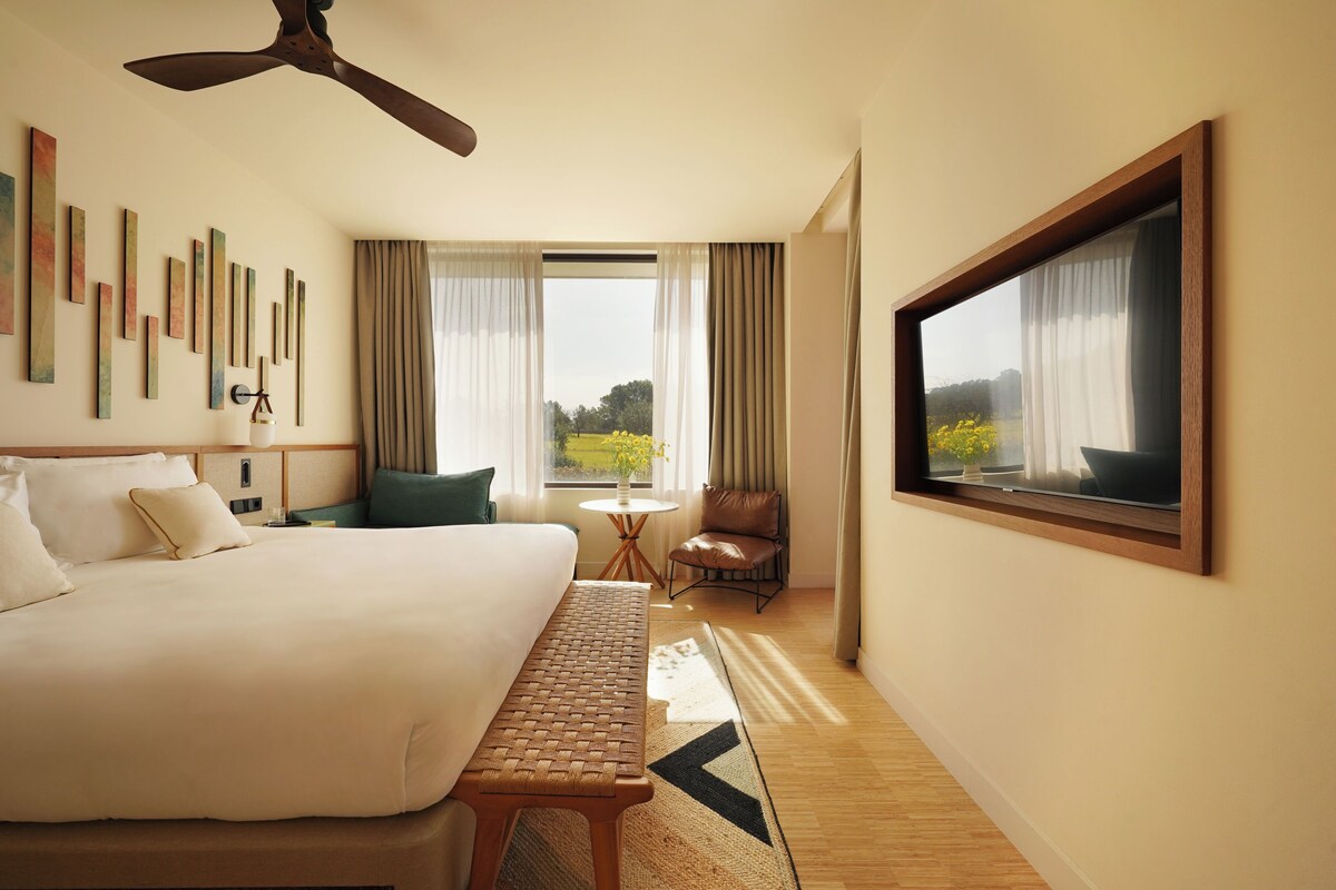 A hotel room with a bed, a desk, a chair, a window with curtains, and a ceiling fan.