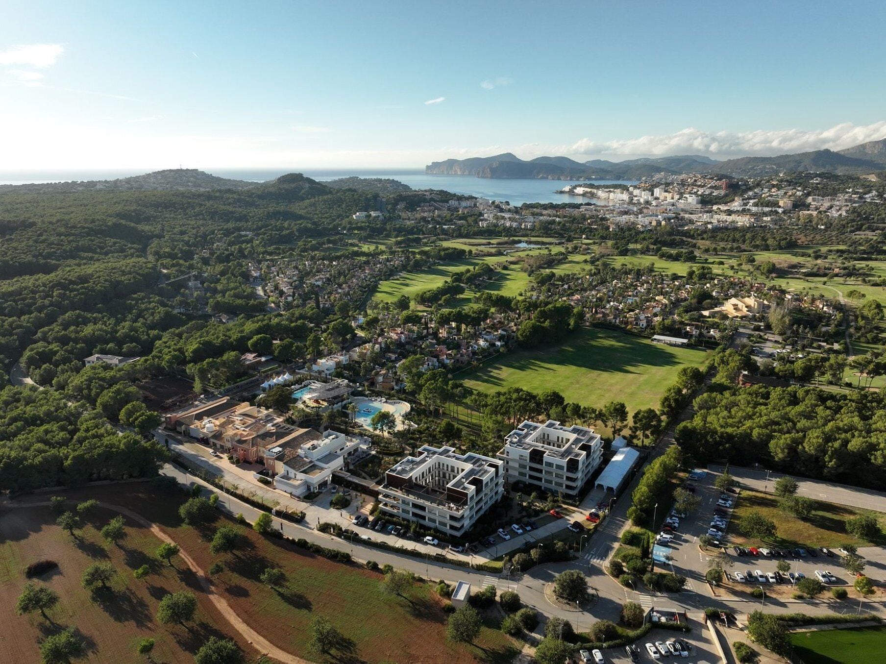 Vista aérea de un pueblo costero con un gran complejo de edificios, zonas verdes y un puerto deportivo.