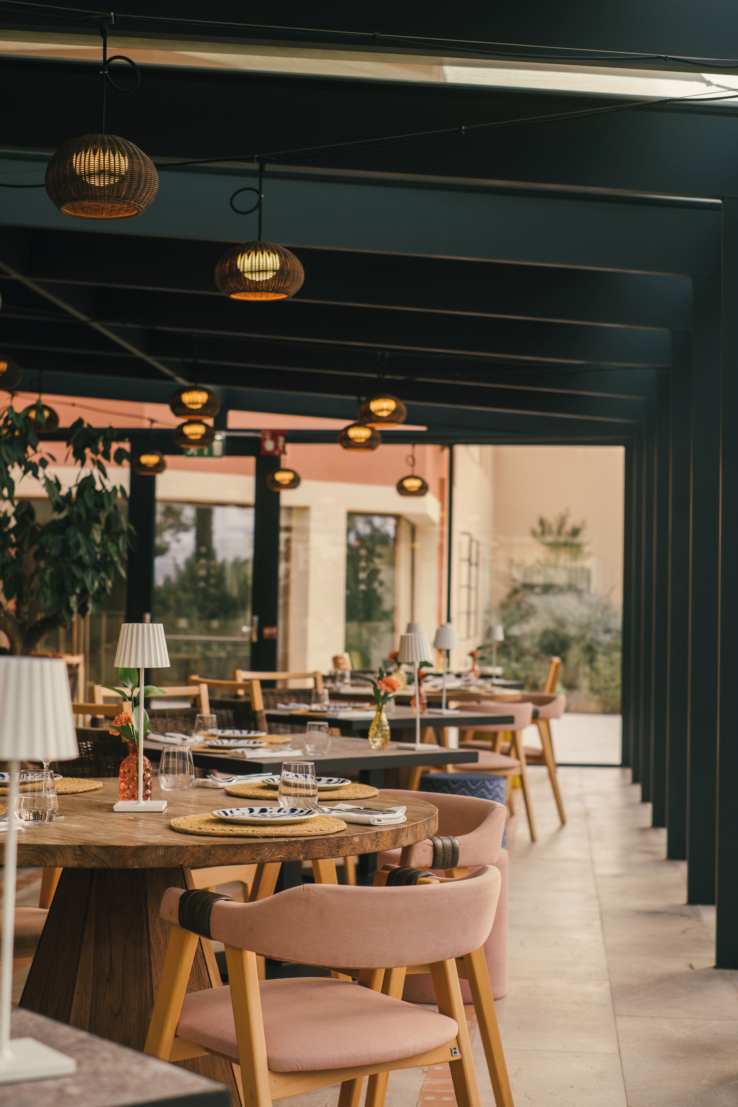 An outdoor dining area with tables and chairs, hanging pendant lights, and a view of the outdoors.