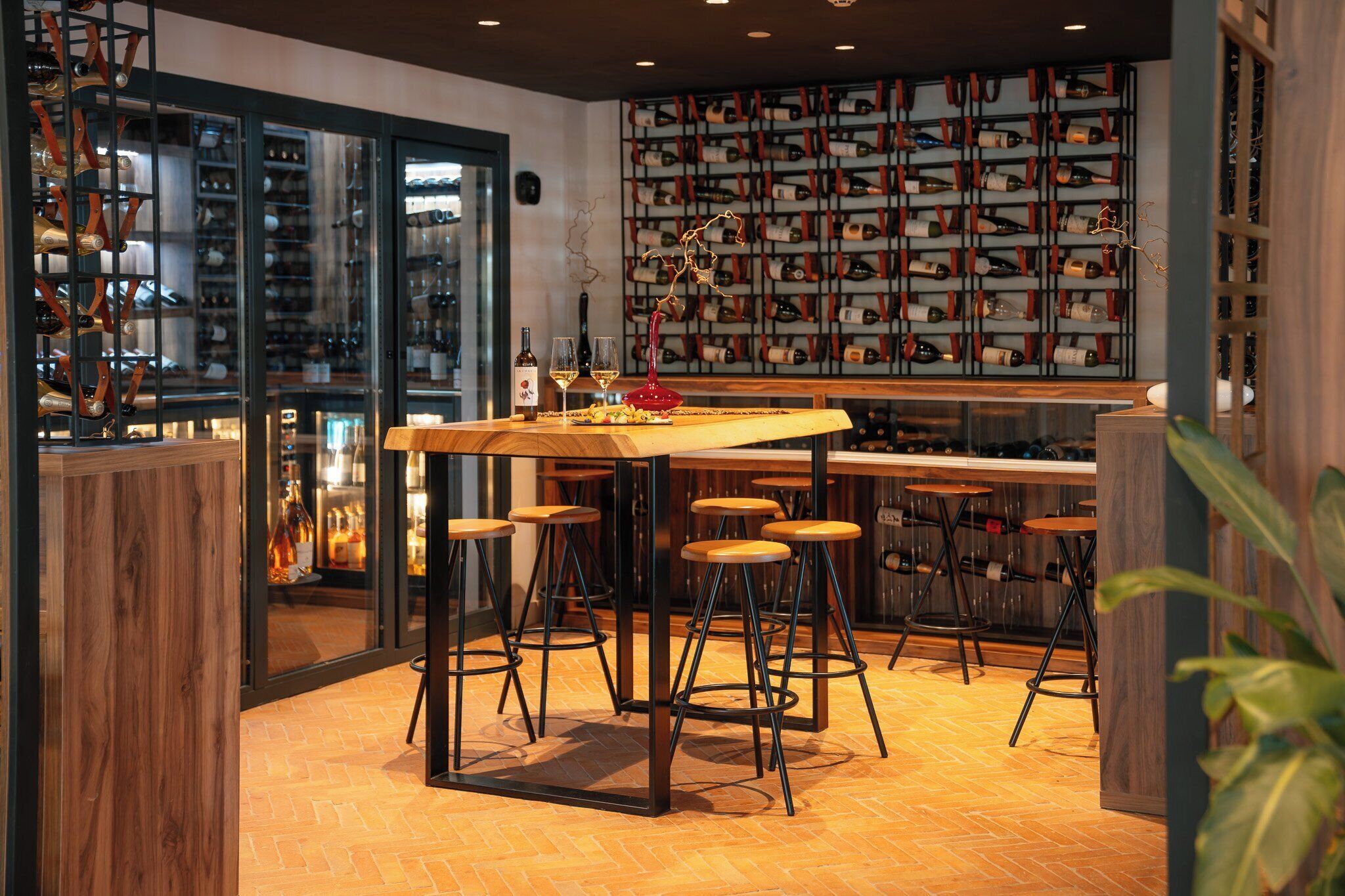 A bar area with stools, a wooden table, and a wine rack in the background.