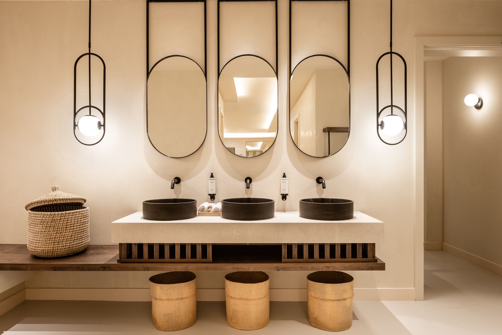 Un baño moderno con dos lavamanos redondos, un espejo grande y tres lámparas colgantes.
