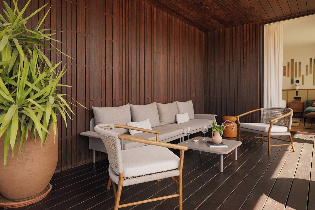 A modern living area with a sofa, two armchairs, a coffee table, and a potted plant.