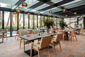 Un restaurante con terraza, ventanas amplias y lámparas colgantes.