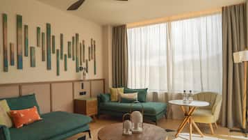 Habitación de hotel moderna con un sofá verde, una mesa redonda de madera y un ventilador de techo.
