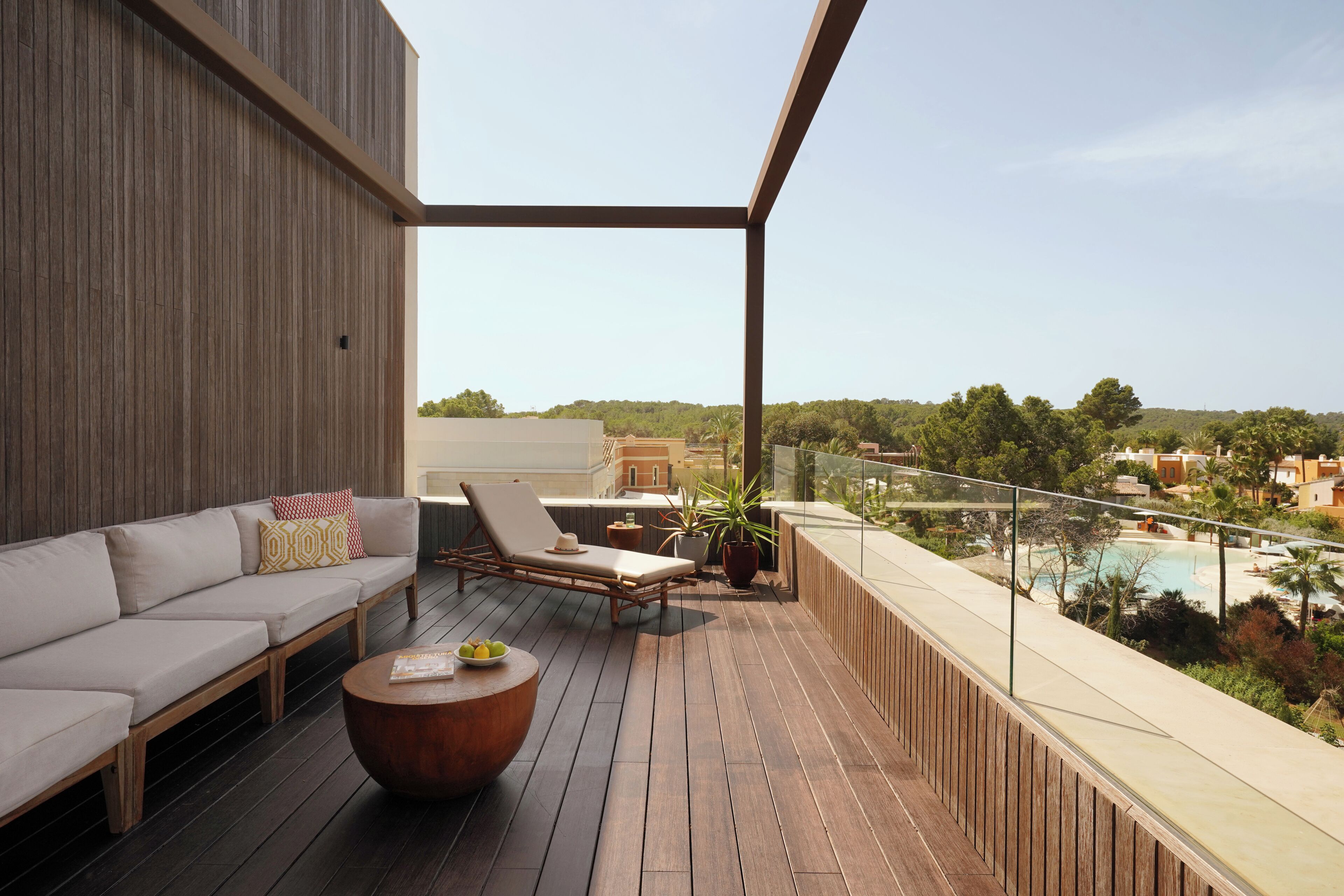 Una terraza de madera con sofá, sillones, una mesa redonda y plantas en macetas.