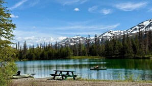 A lake with a boat, a picnic table, and snow-capped mountains in the background.