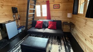 A cozy cabin interior with a sofa, a small table, a lamp, a ladder, and a power outlet on the wall.