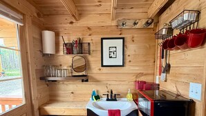 A compact kitchen with wooden walls, a sink, a microwave, and a trash bin.