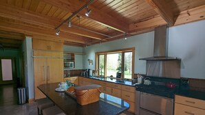 Een moderne keuken met houten kastjes, een centraal eiland, roestvrijstalen apparatuur en een groot raam dat voor natuurlijk licht zorgt.