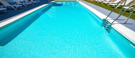 Una piscina con agua azul cristalina, rodeada de sillas de descanso blancas y una escalera metálica.
